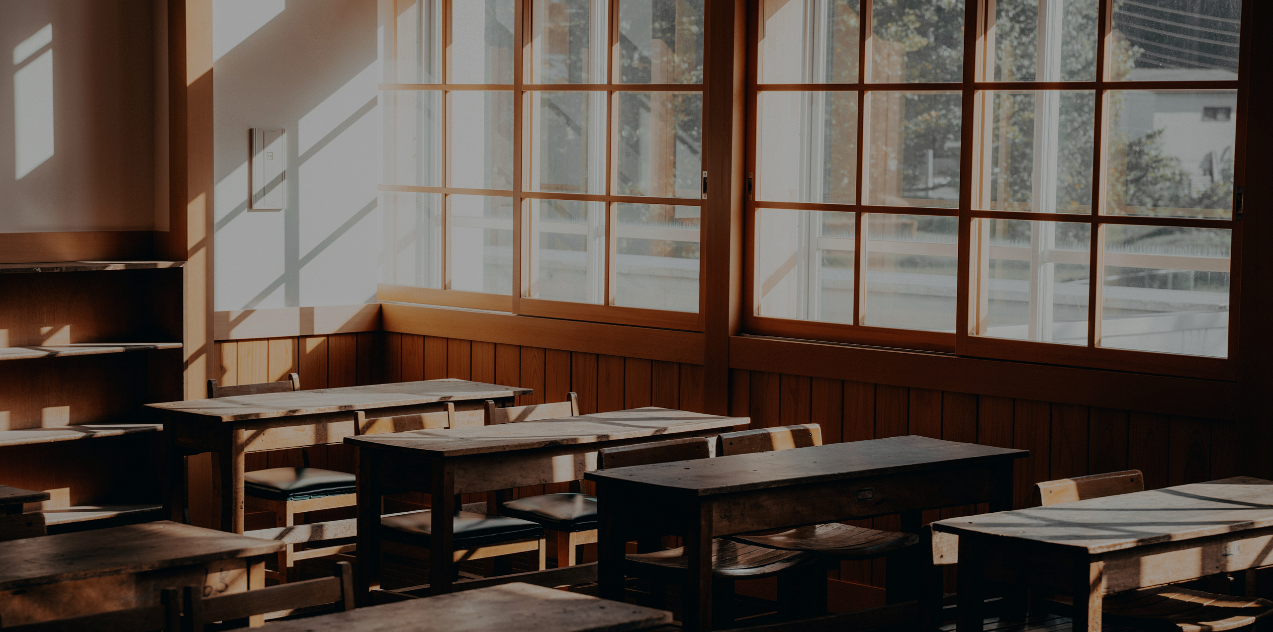 Photo of a elementary school classroom with wmpty wooden desks and sun shining through the windows.